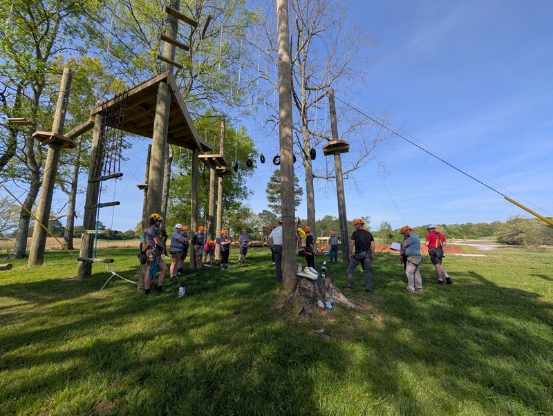 Image of 15 new staff standing under a ropes course during staff training